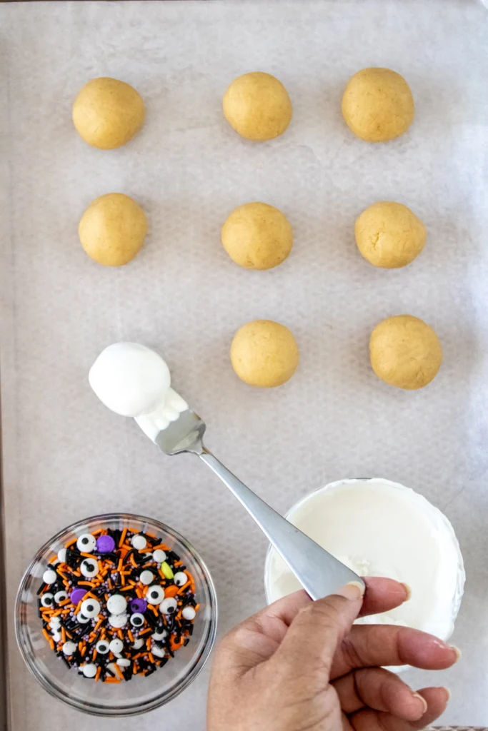 Freshly coated cake truffle being set onto parchment paper next to un-dipped cake balls