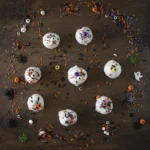 Top down view of Halloween cake truffles on a dark wood background with colorful spooky sprinkles scattered around