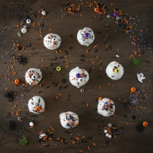 Top down view of Halloween cake truffles on a dark wood background with colorful spooky sprinkles scattered around