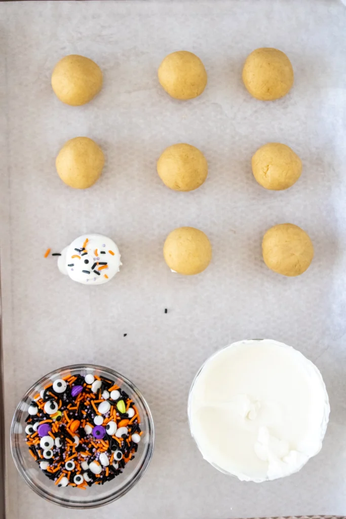 One decorated cake truffle covered in Halloween sprinkles sitting among un-dipped cake balls on parchment paper.