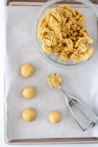 Small cookie scoop on a parchment lined tray with rolled cake balls arranged and ready to be dipped.