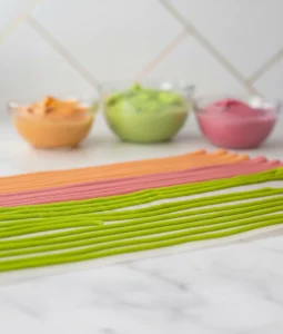 Bright homemade sprinkle icing lines in green, pink, and orange drying on parchment paper