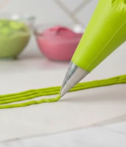 Green icing being piped onto parchment paper using a small round piping tip to create homemade sprinkles