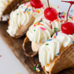 Banana split tacos made with waffle cone shells filled with creamy homemade banana ice cream topped with whipped cream and sprinkles.
