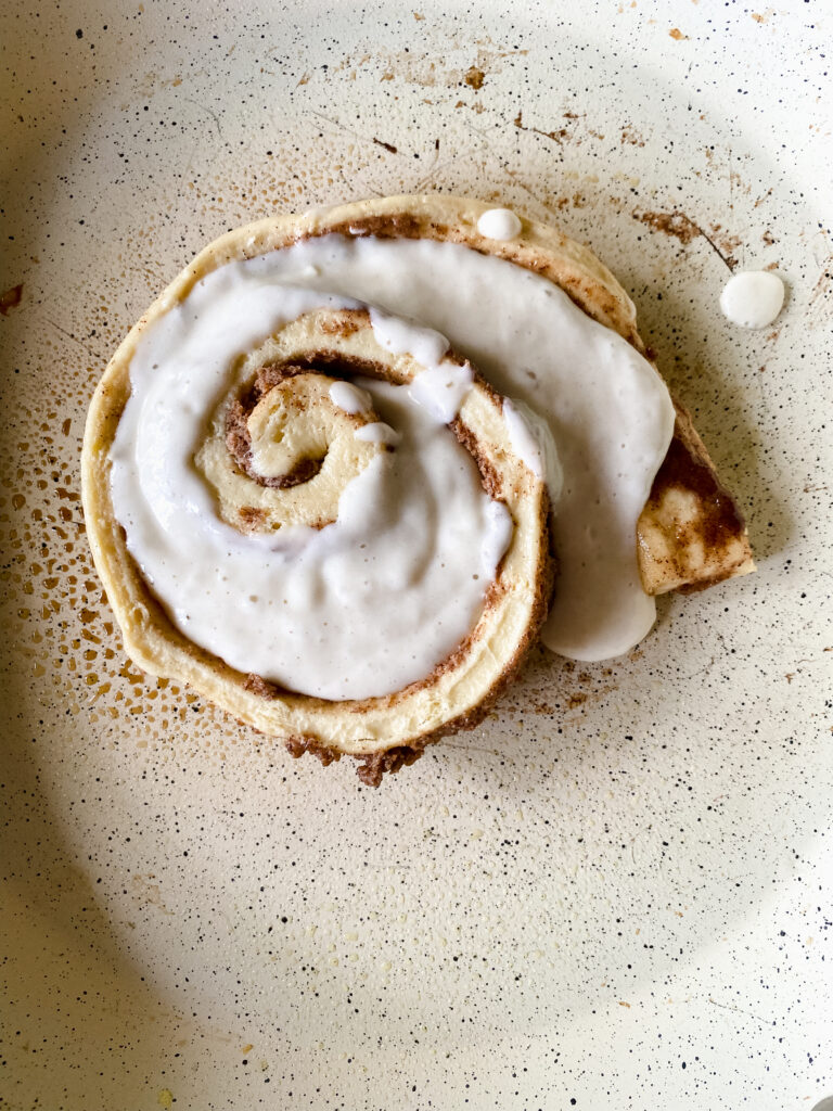 Pancake batter filling the gaps of a loosely wrapped cinnamon roll in a skillet.