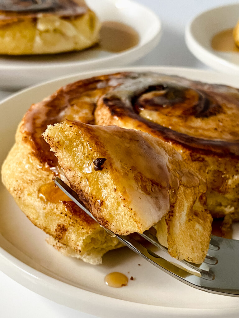 Fork holding a bite of an easy cinnamon roll pancake topped with icing and maple syrup.