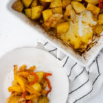 Seasoned breakfast potatoes baked with onions and bell peppers in a casserole dish with a serving plated beside it.