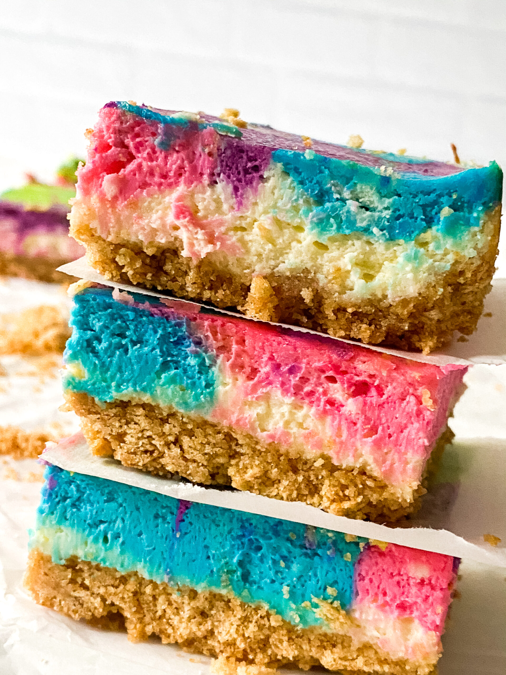 Colorful unicorn cheesecake bars with pink, blue, and purple swirls on a graham cracker crust.