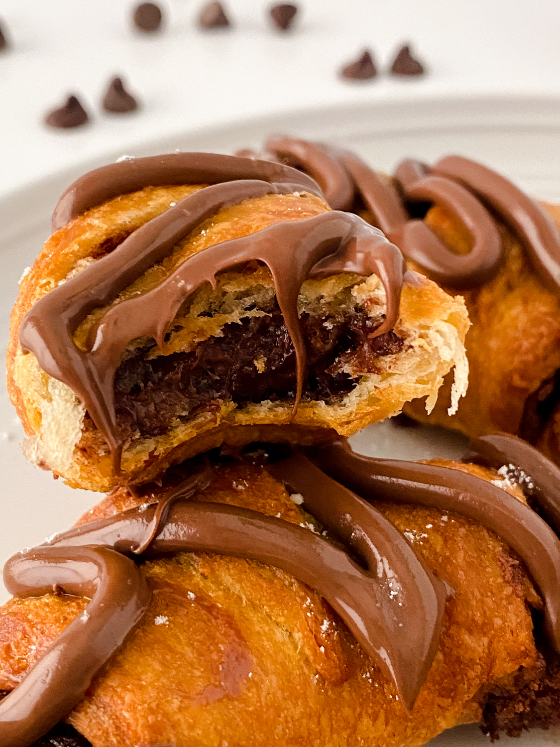 Warm Nutella stuffed crescent rolls drizzled with chocolate sauce and served on a white plate.
