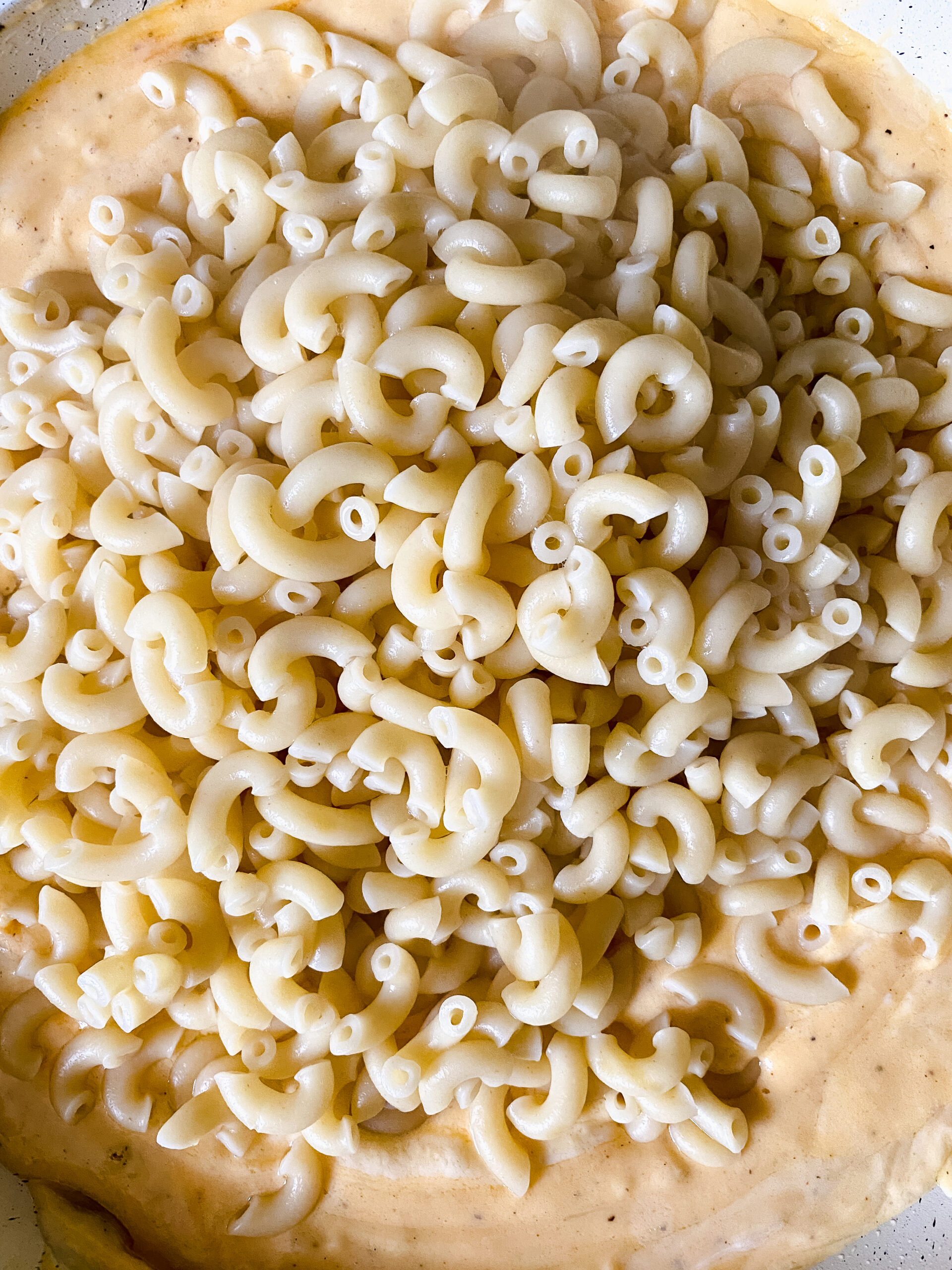 Cooked elbow macaroni being added to a creamy homemade cheese sauce for baked macaroni and cheese.
