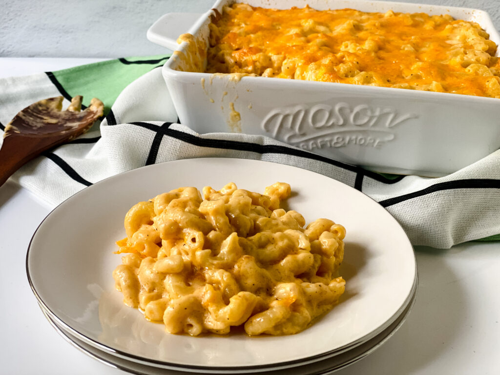 Easy baked macaroni and cheese served on a white plate with a casserole dish of creamy baked mac and cheese in the background.