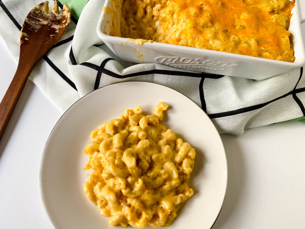 Easy baked macaroni and cheese served on a plate with a baking dish of creamy macaroni and cheese in the background.
