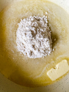 Flour being added to melted butter in a skillet to make a roux for homemade baked macaroni and cheese.