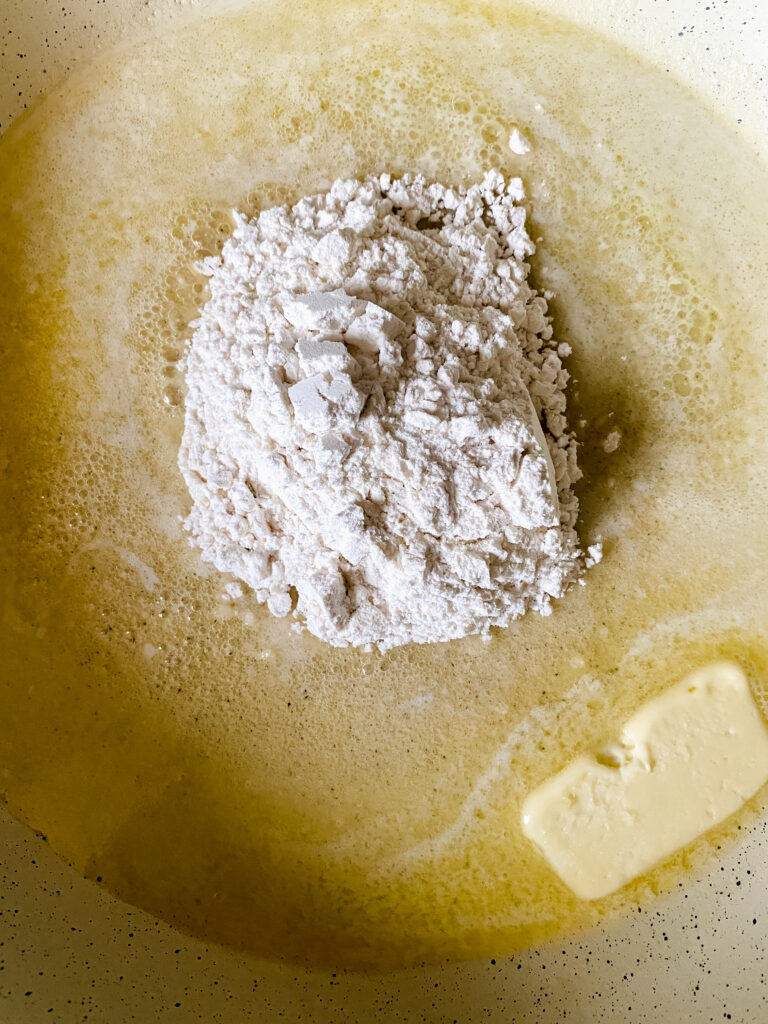 Flour being added to melted butter in a skillet to make a roux for homemade baked macaroni and cheese.