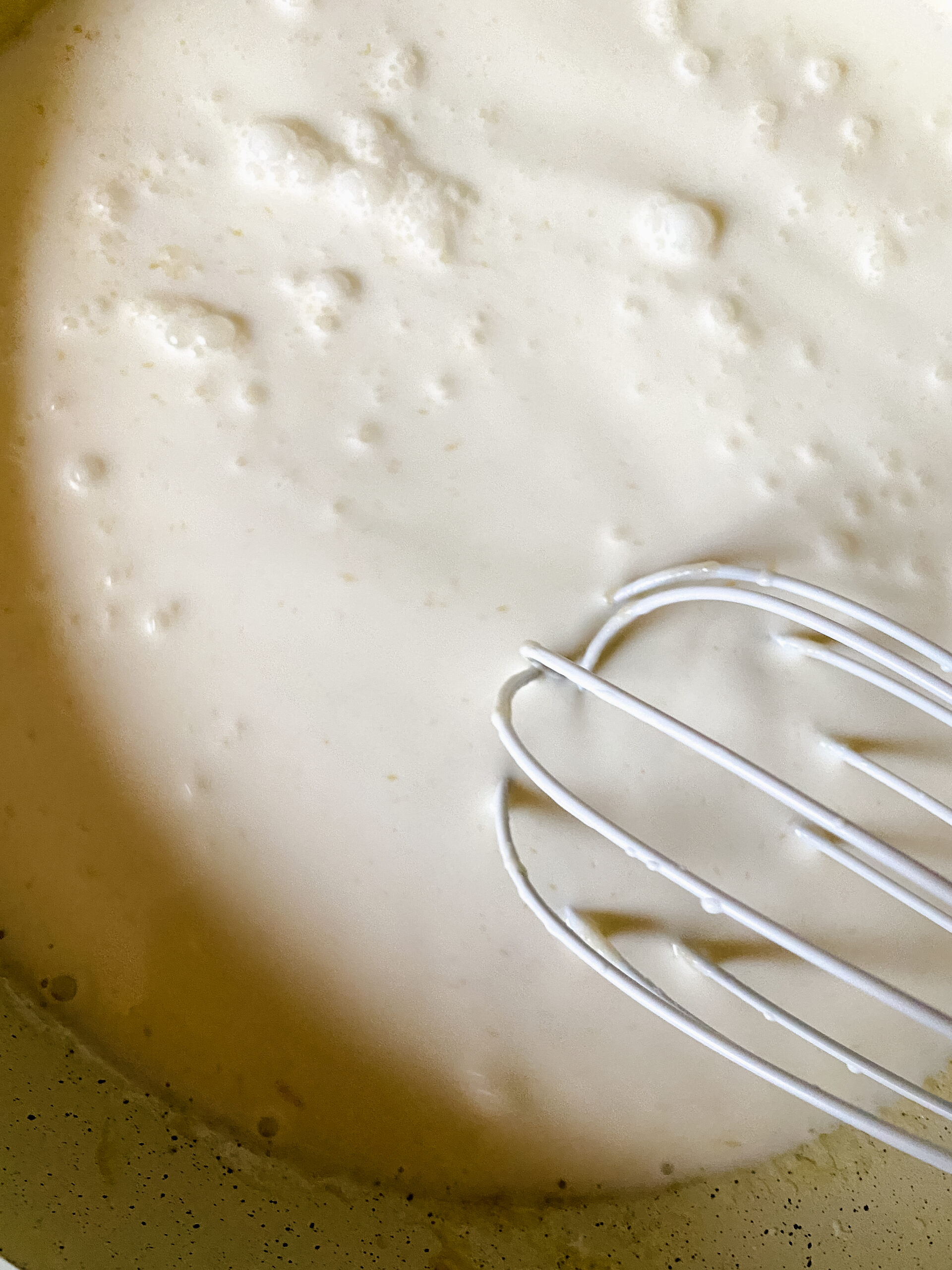 Milk and cream being whisked into a roux to create the base for a homemade cheese sauce.