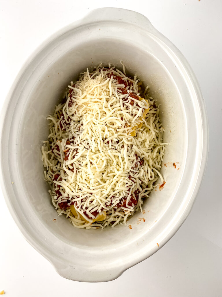 Shredded mozzarella and Parmesan cheese layered over meat sauce, lasagna noodles, and ravioli in a crock pot lasagna.