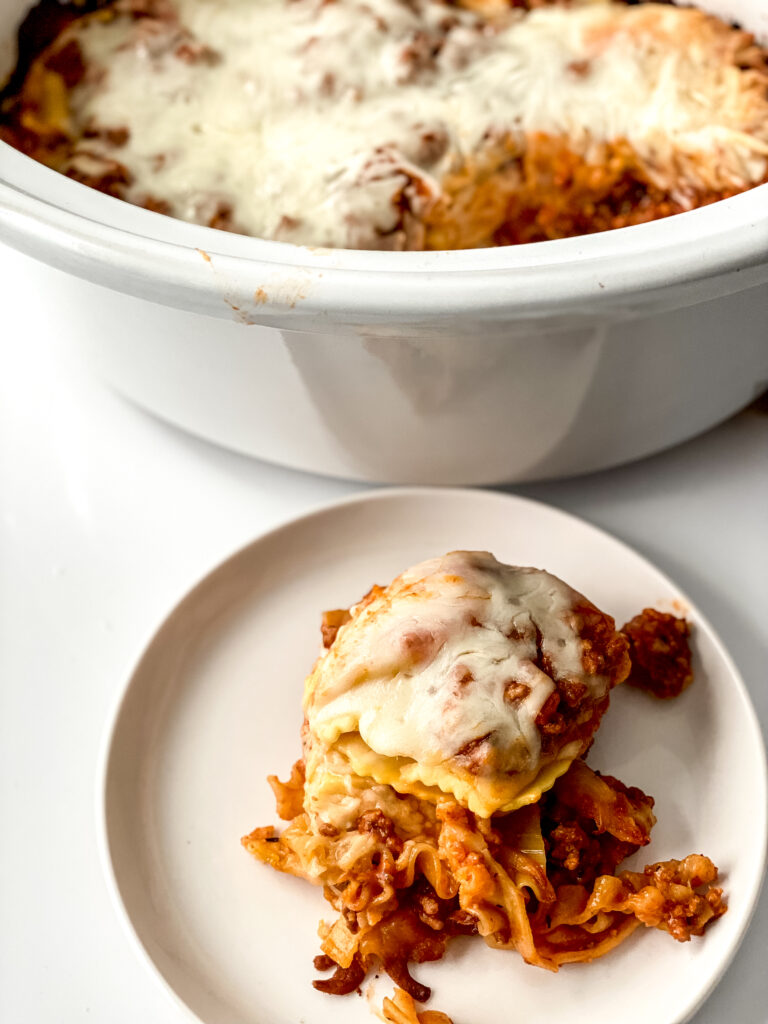 Finished crock pot lasagna with a plated serving showing cheesy layers beside the slow cooker.