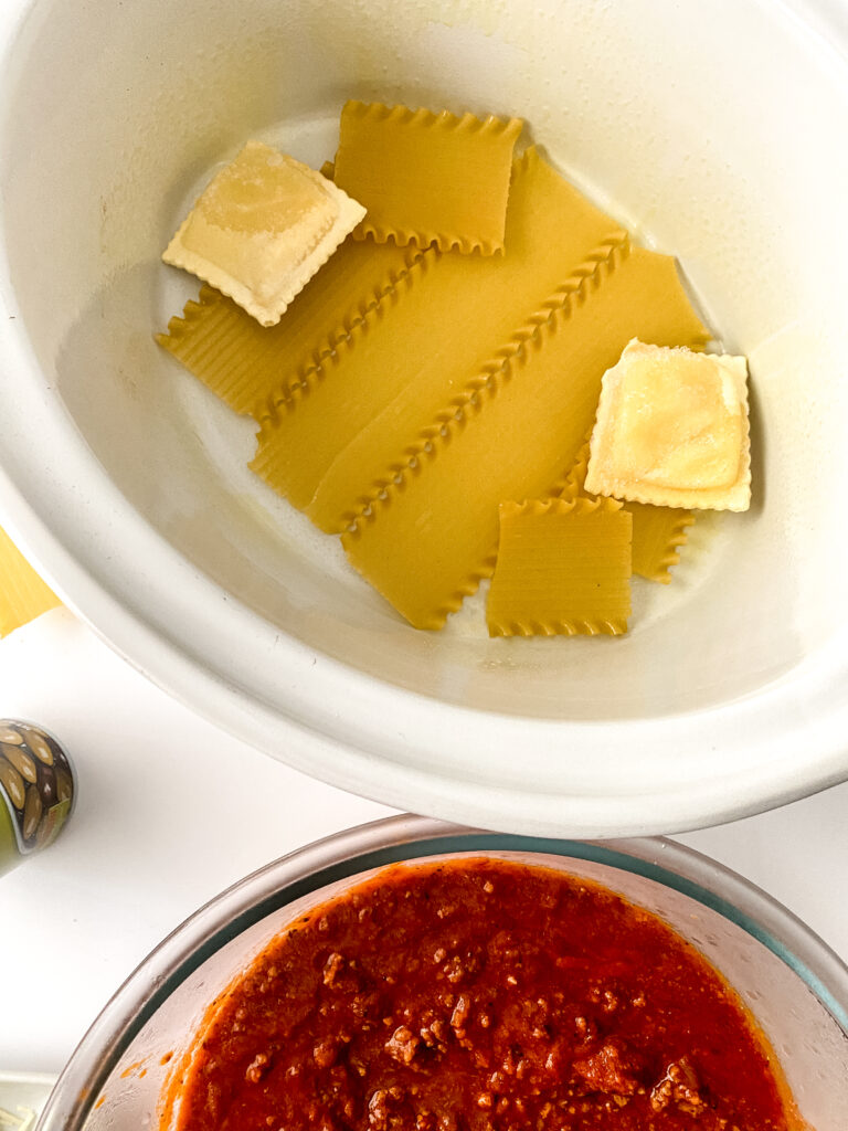 Oven-ready lasagna noodles and frozen cheese ravioli arranged in the bottom of a slow cooker for the first layer of easy crock pot lasagna.