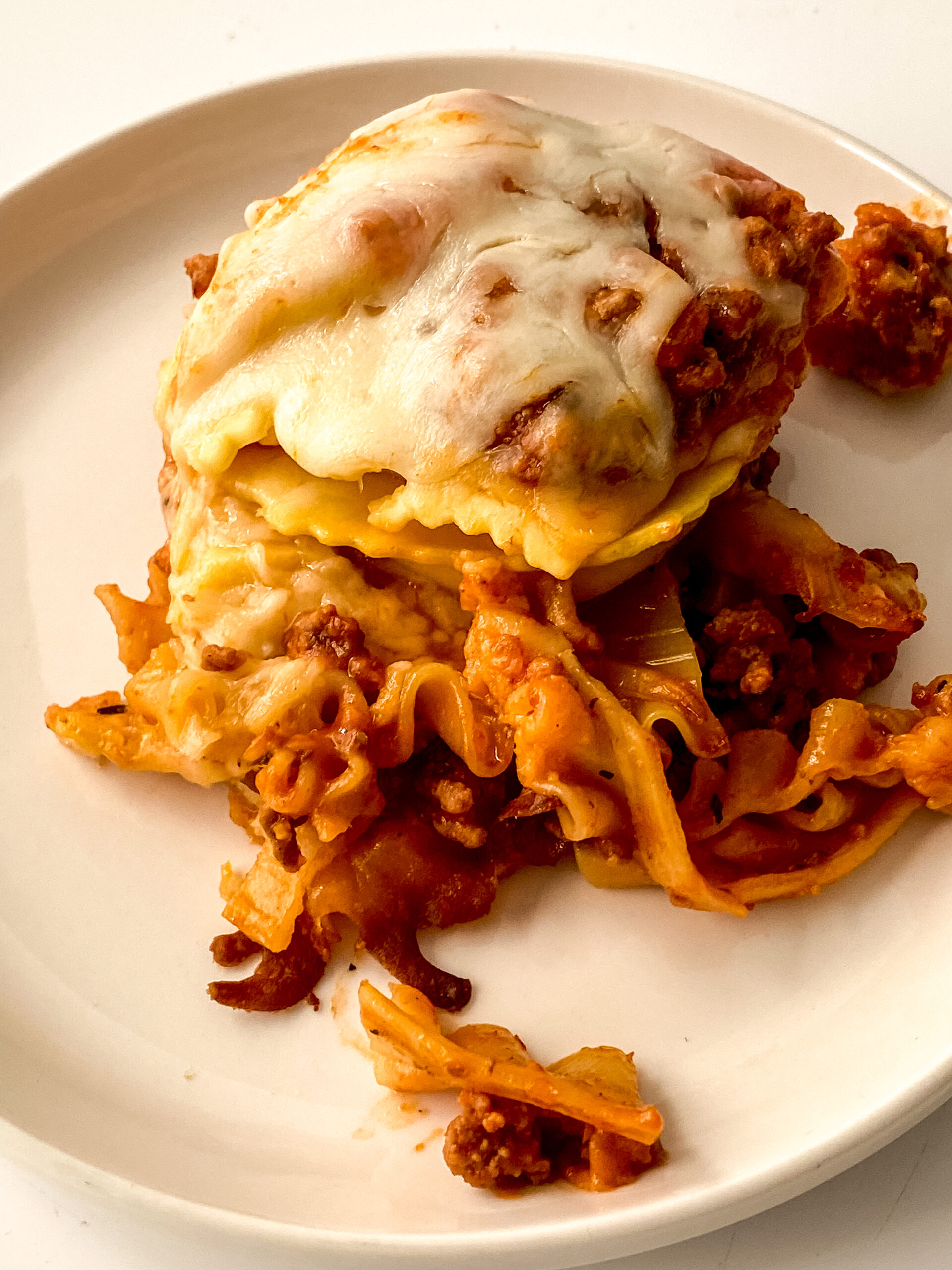 A plated serving of crock pot lasagna with melted mozzarella cheese, oven-ready noodles, frozen ravioli, and hearty meat sauce.