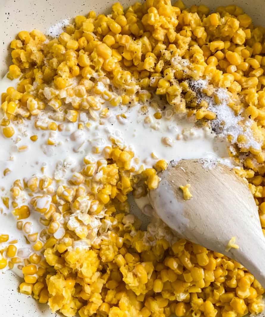 Frozen corn, heavy cream, salt, pepper, and sugar added to a saucepan and stirred together to begin making homemade creamed corn.