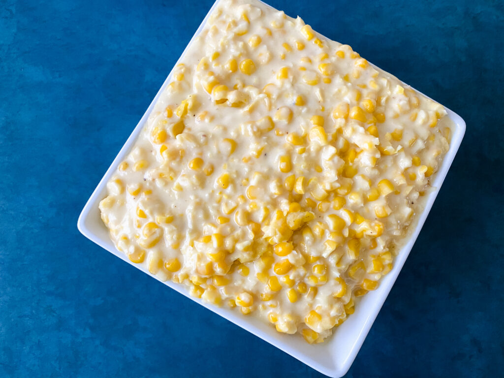 Easy creamed corn with frozen corn served in a white bowl on a blue background.