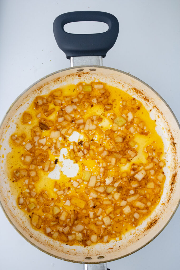 Softened onions cooking in butter and pan drippings in a skillet for one pot chicken and rice.