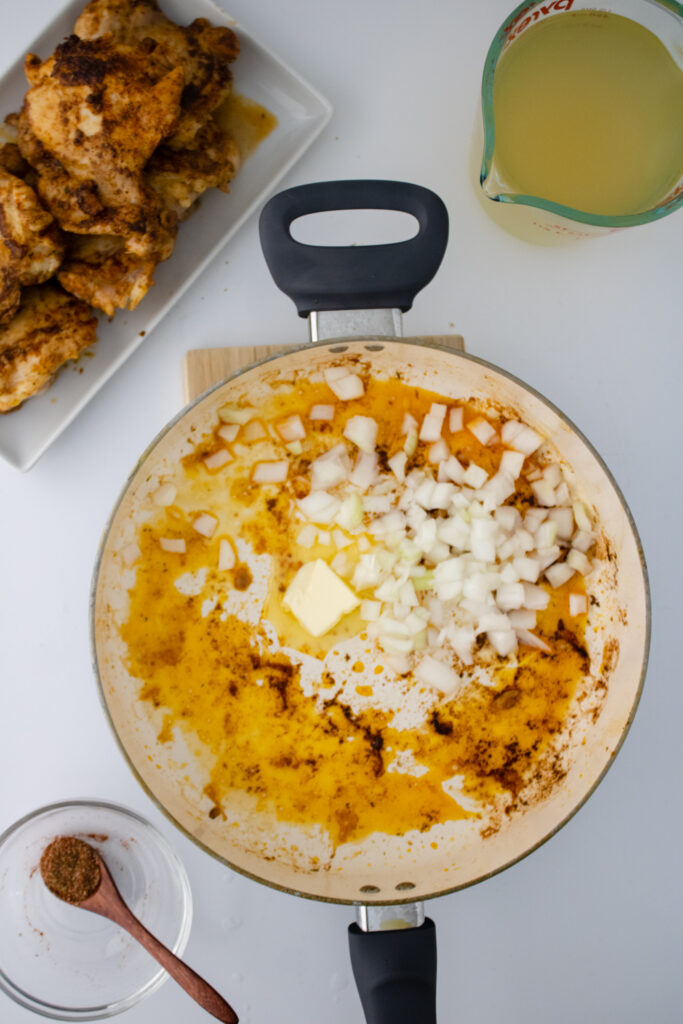 Chopped onions and butter being added to a skillet after searing chicken for one pot chicken and rice.