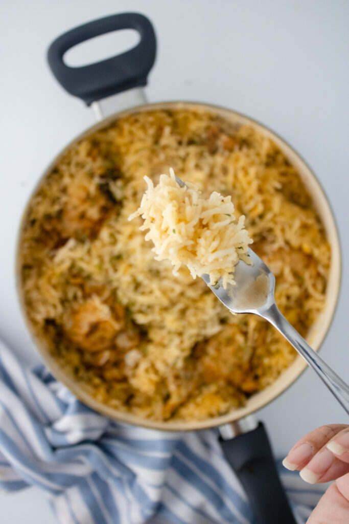 Fork holding a bite of fluffy basmati rice above a skillet of one pot chicken and rice.