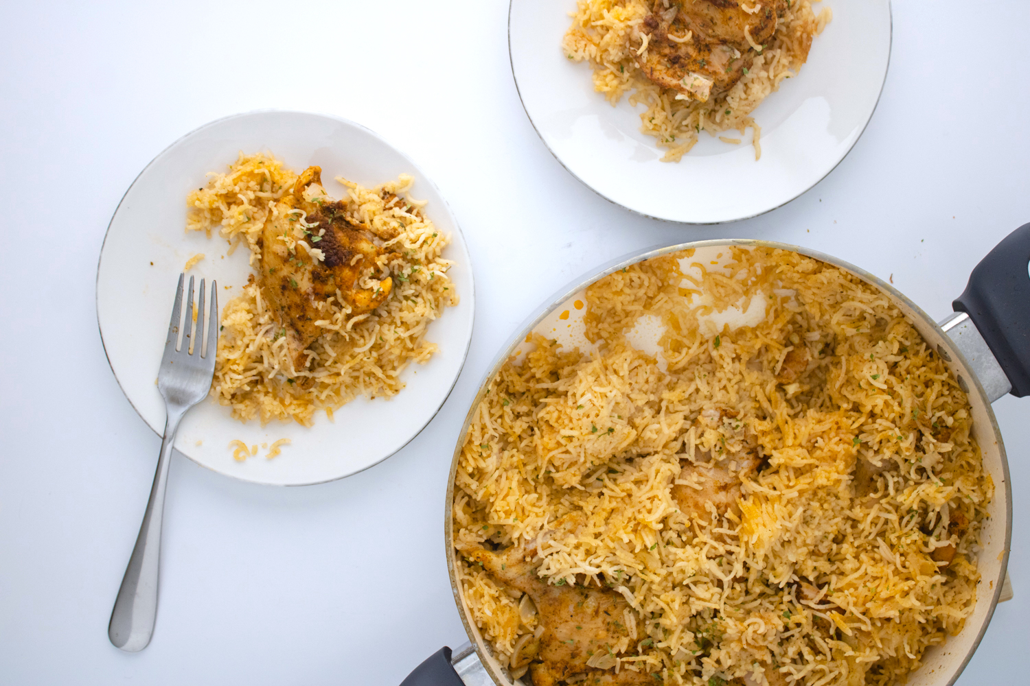 One pot chicken and rice made with seasoned chicken thighs and fluffy basmati rice served directly from a large skillet with plated portions ready to enjoy.