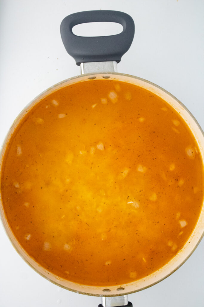 Seasoned chicken broth, rice, and onions combined in a skillet before adding the chicken back to the pan.
