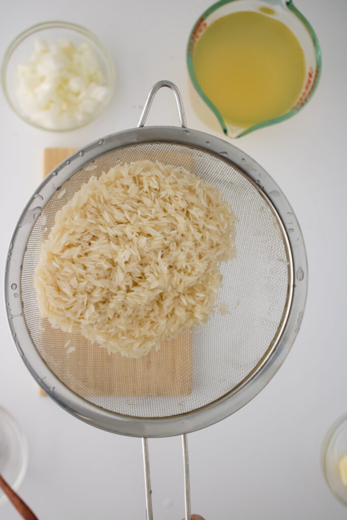 Basmati rice being rinsed in a fine mesh strainer before making one pot chicken and rice.