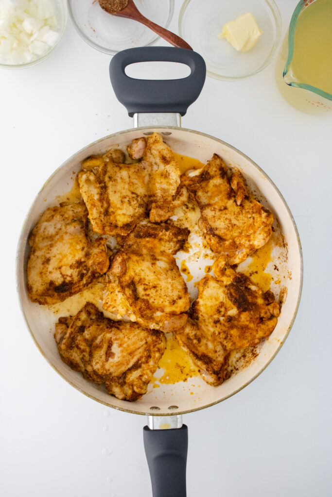 Seasoned chicken thighs searing in a skillet before cooking one pot chicken and rice with basmati rice.