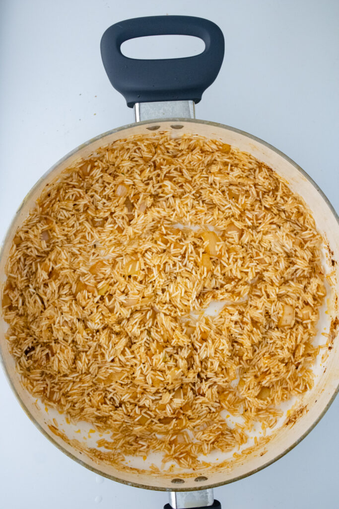 Basmati rice coated with seasonings and onions while toasting in a skillet for one pot chicken and rice.