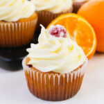 Cranberry orange cupcake topped with orange buttercream frosting and a sugared cranberry garnish.