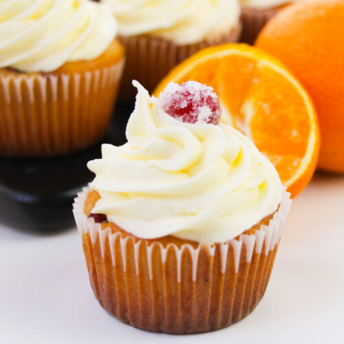 Cranberry orange cupcake topped with orange buttercream frosting and a sugared cranberry garnish.
