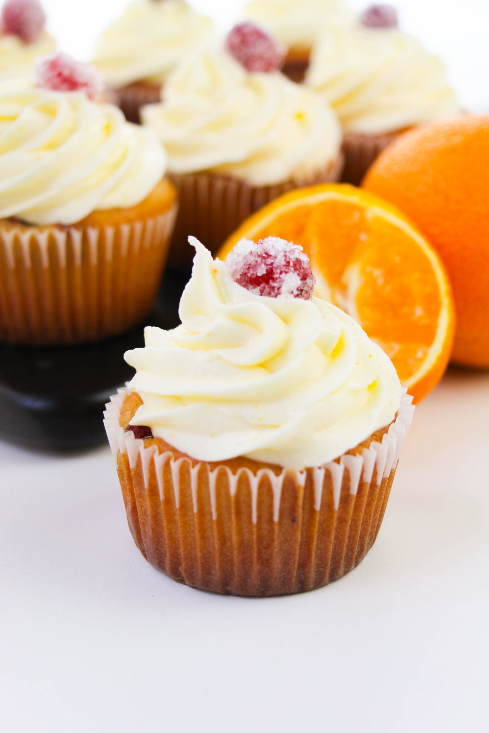 Cranberry orange cupcake topped with orange buttercream frosting and a sugared cranberry garnish.