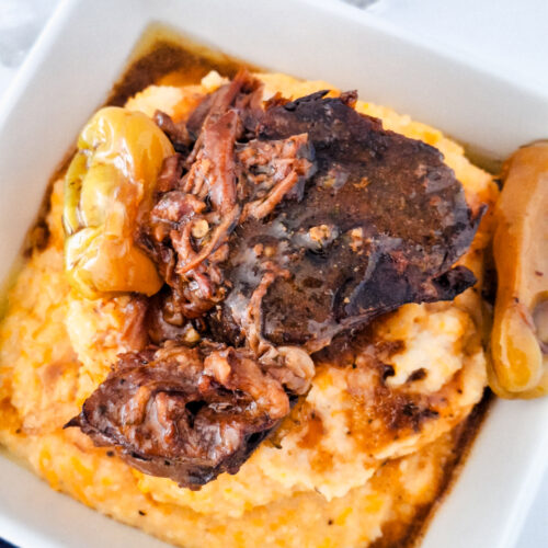 Square bowl filled with tender Mississippi pot roast resting on a bed of creamy sweet potato grits.
