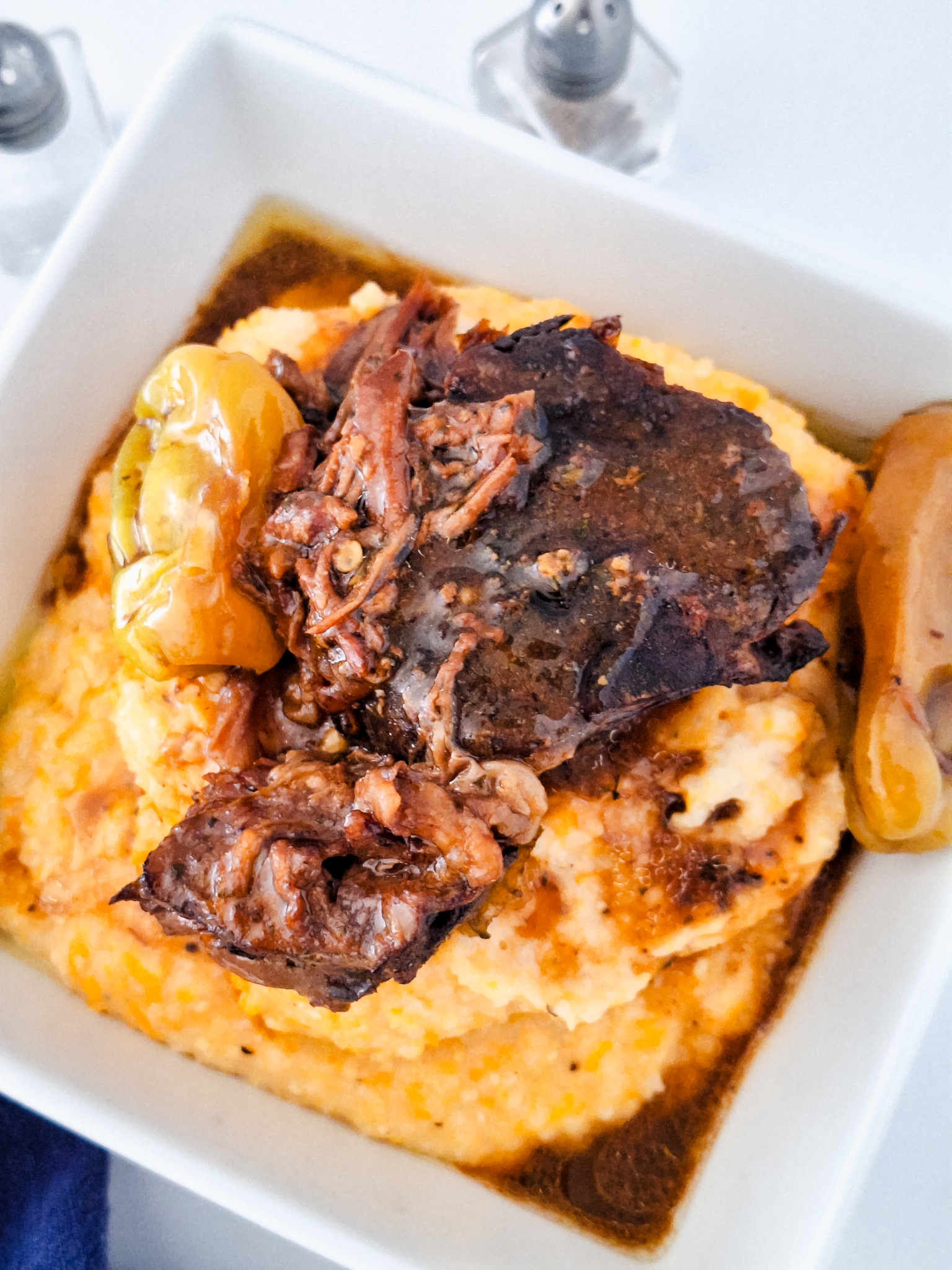 Square bowl filled with tender Mississippi pot roast resting on a bed of creamy sweet potato grits.