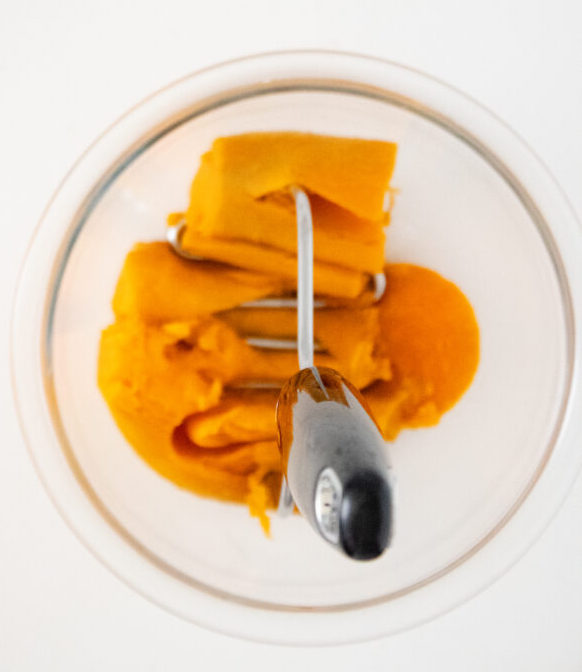 Roasted sweet potato being mashed with a potato masher for sweet potato grits