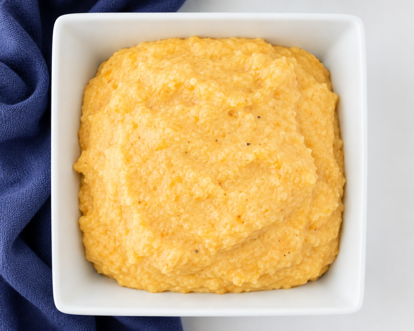 Close-up of creamy sweet potato grits served in a white bowl with a blue cloth in the background.