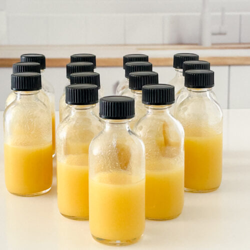 Forward-facing image of small glass bottles filled with golden pineapple ginger shots arranged in a triangle on a white surface.