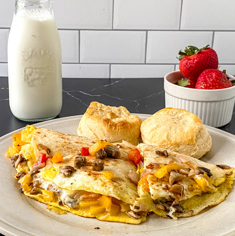 Veggie breakfast quesadilla filled with eggs, bell peppers, onions, and melted cheese served with biscuits and fresh strawberries.