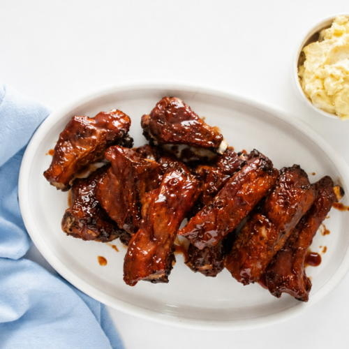 Air fryer baby back ribs coated in barbecue sauce and served on a white platter with a side of mashed potatoes.
