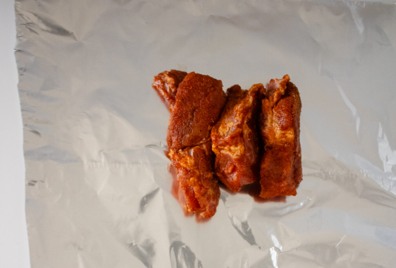 Seasoned baby back rib sections arranged on a sheet of aluminum foil before being wrapped and cooked in the air fryer.