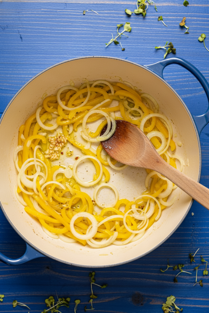 Overhead photo of onions, yellow bell peppers, and garlic sautéing in a Dutch oven for Southern-style frozen baby lima beans.