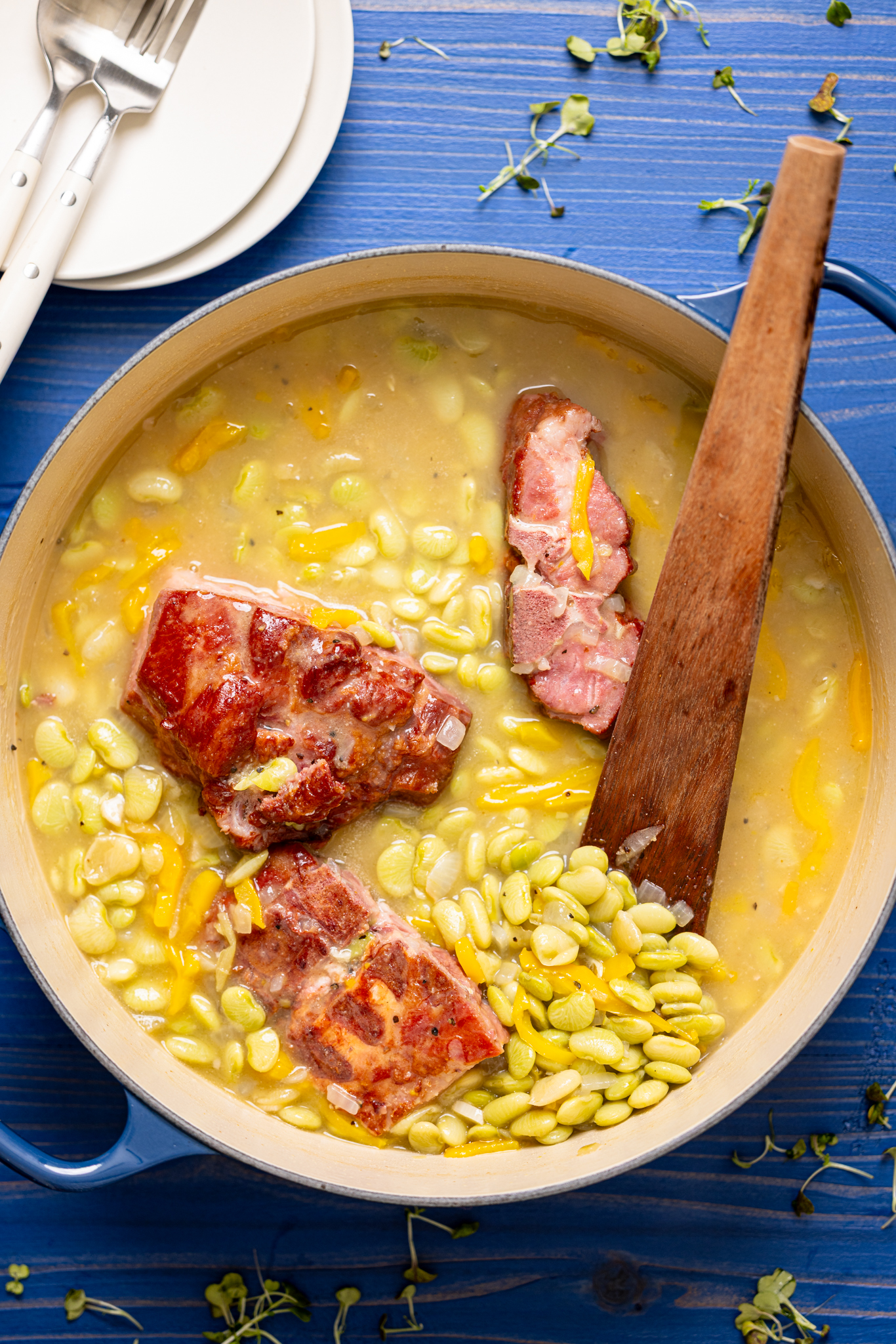 Overhead photo of Southern-style frozen baby lima beans simmering in a pot with ham bone, onions, and bell peppers in a rich, buttery broth.