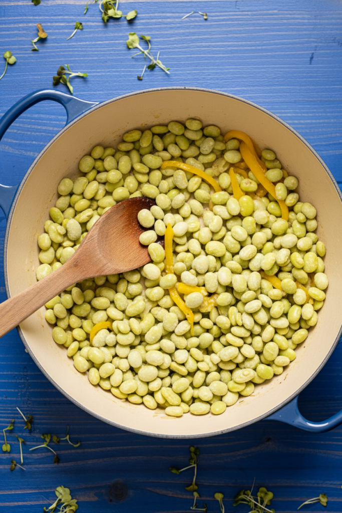 Frozen baby lima beans added to sautéed onions and yellow bell peppers in a Dutch oven during the cooking process.