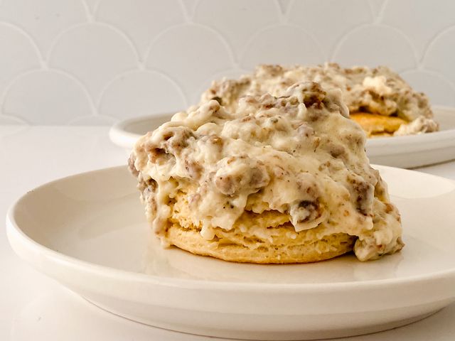 Fluffy buttermilk biscuit topped with creamy sausage gravy on a white plate.