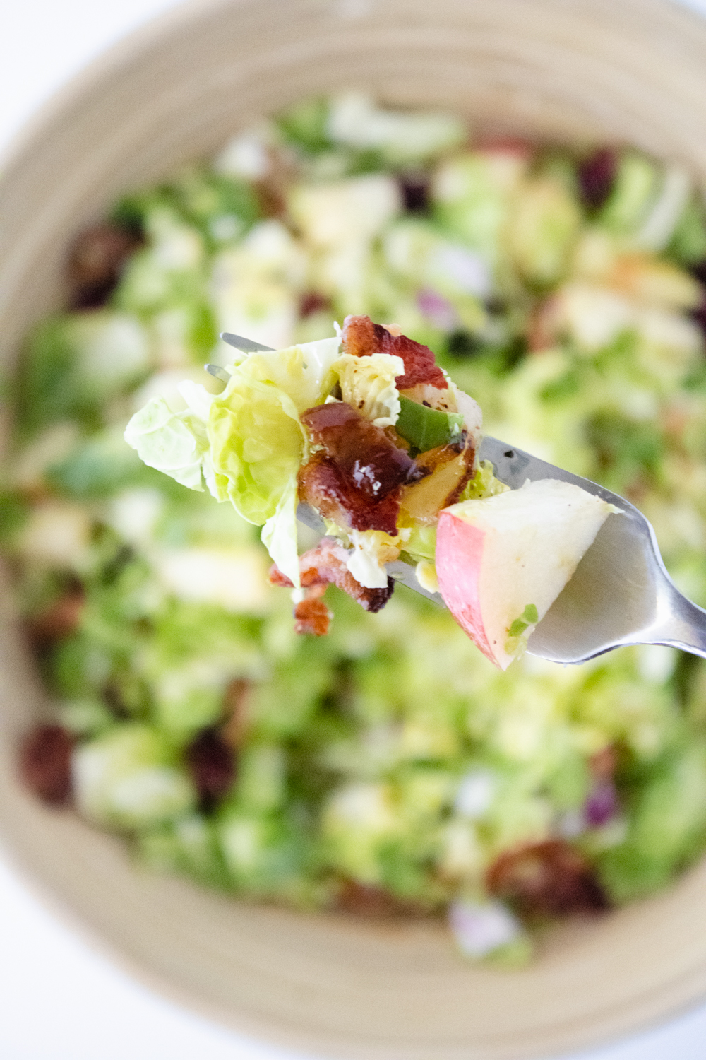 Brussels sprout salad with apples, bacon, red onion, and maple dressing on a fork above a salad bowl.