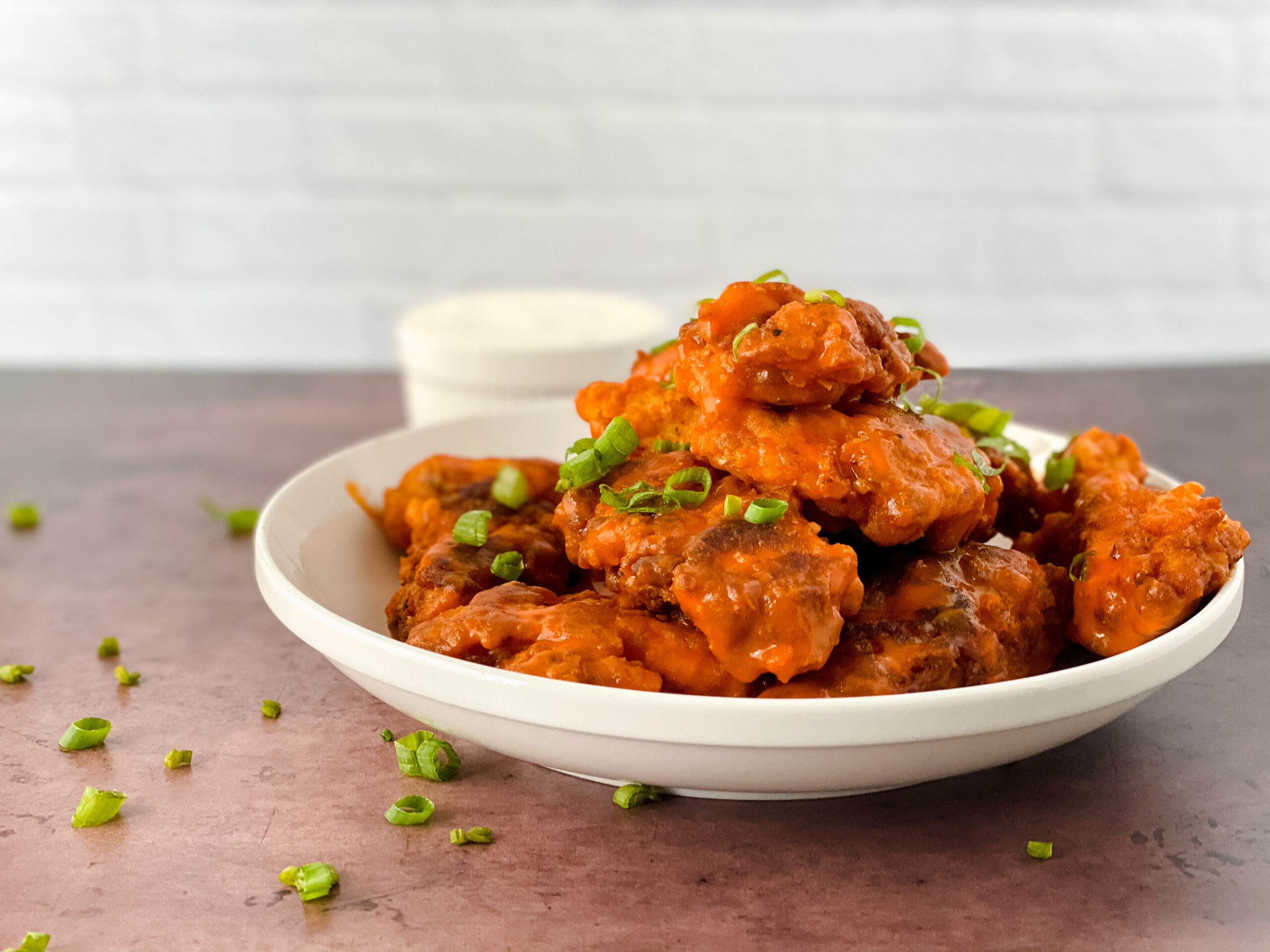 Crispy buffalo chicken tenders coated in spicy buffalo sauce and topped with sliced green onions on a white plate.